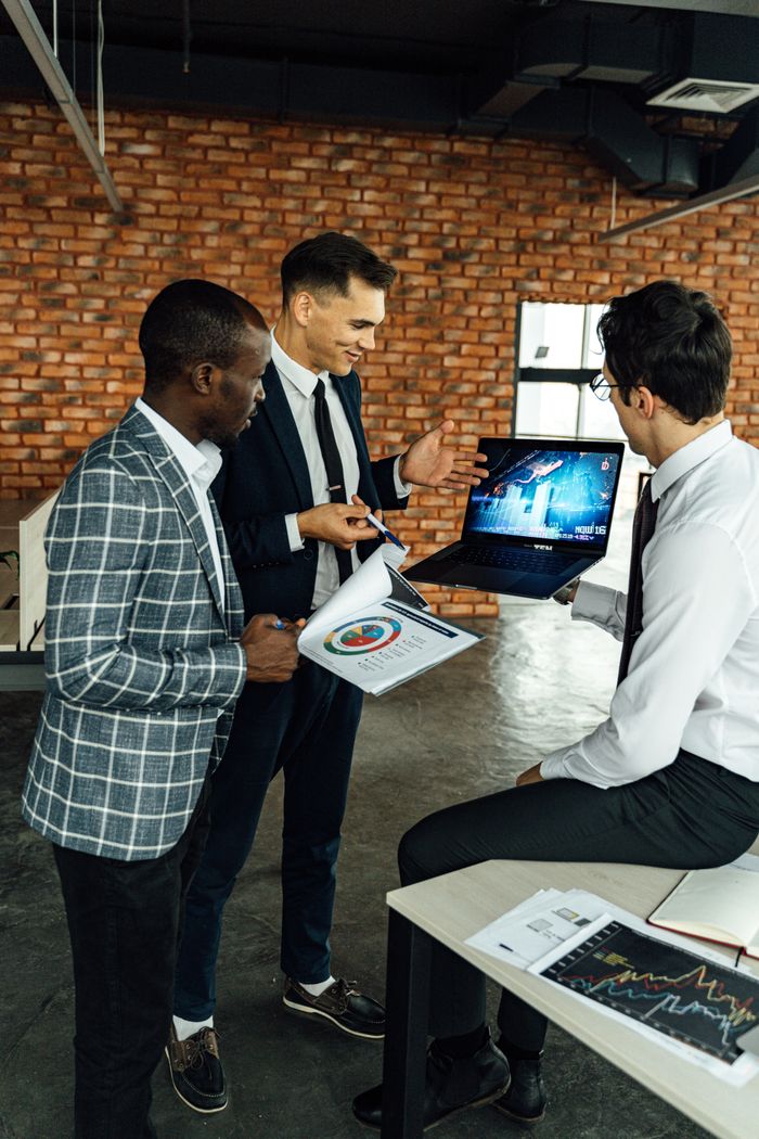 About Three business professionals discussing financial charts in a modern office setting.